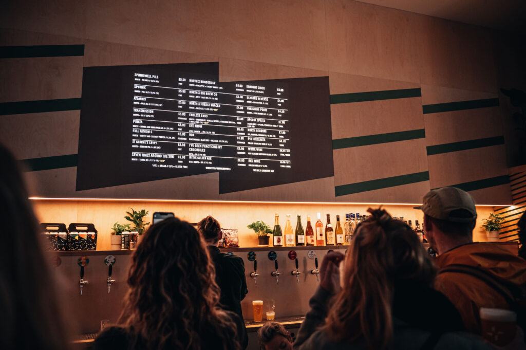 Contemporary bar featuring illuminated shelving and a backlit menu board, with subtle electrical wiring and lighting installations creating a modern and inviting atmosphere.